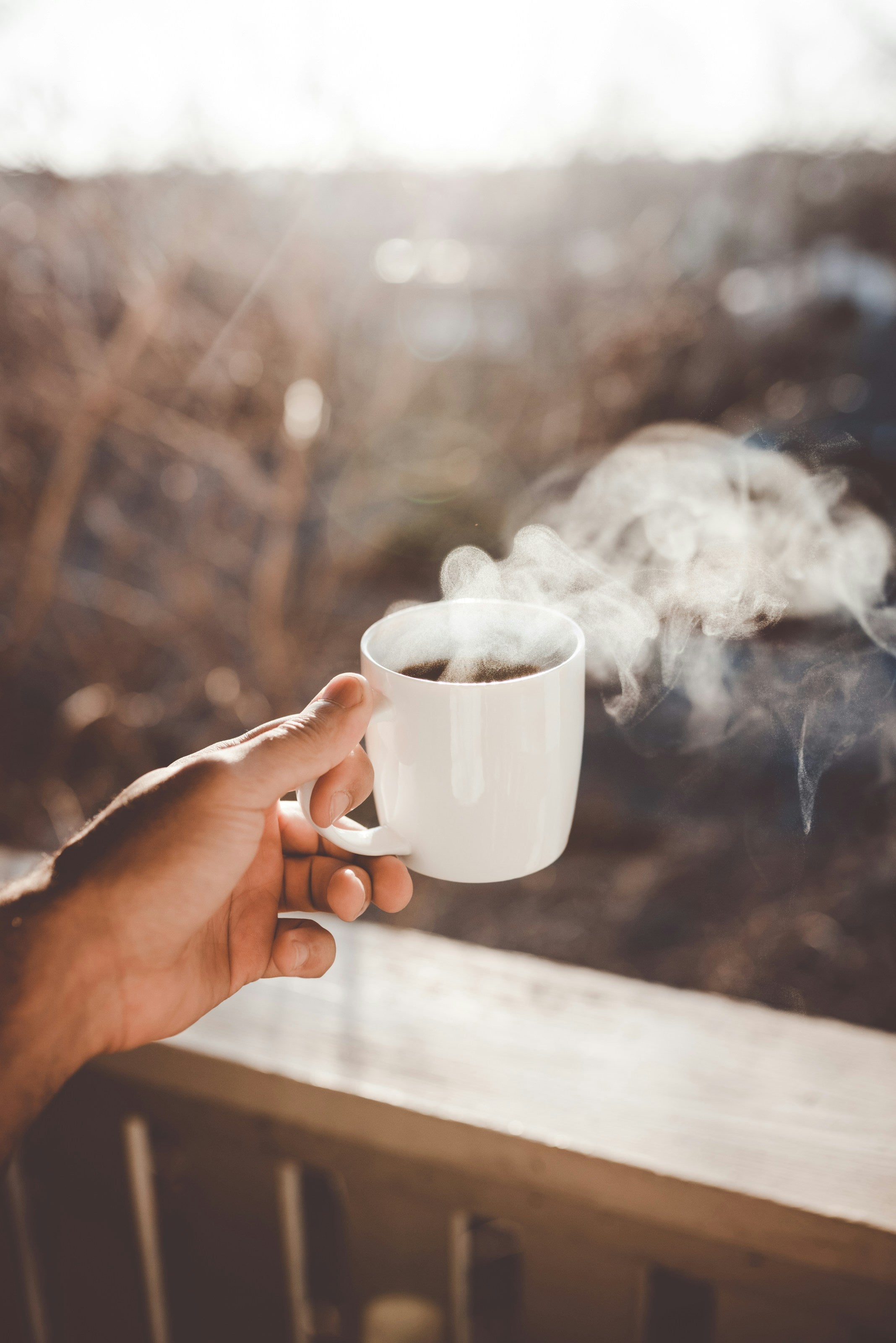 person holding a cup of coffee outside on a deck