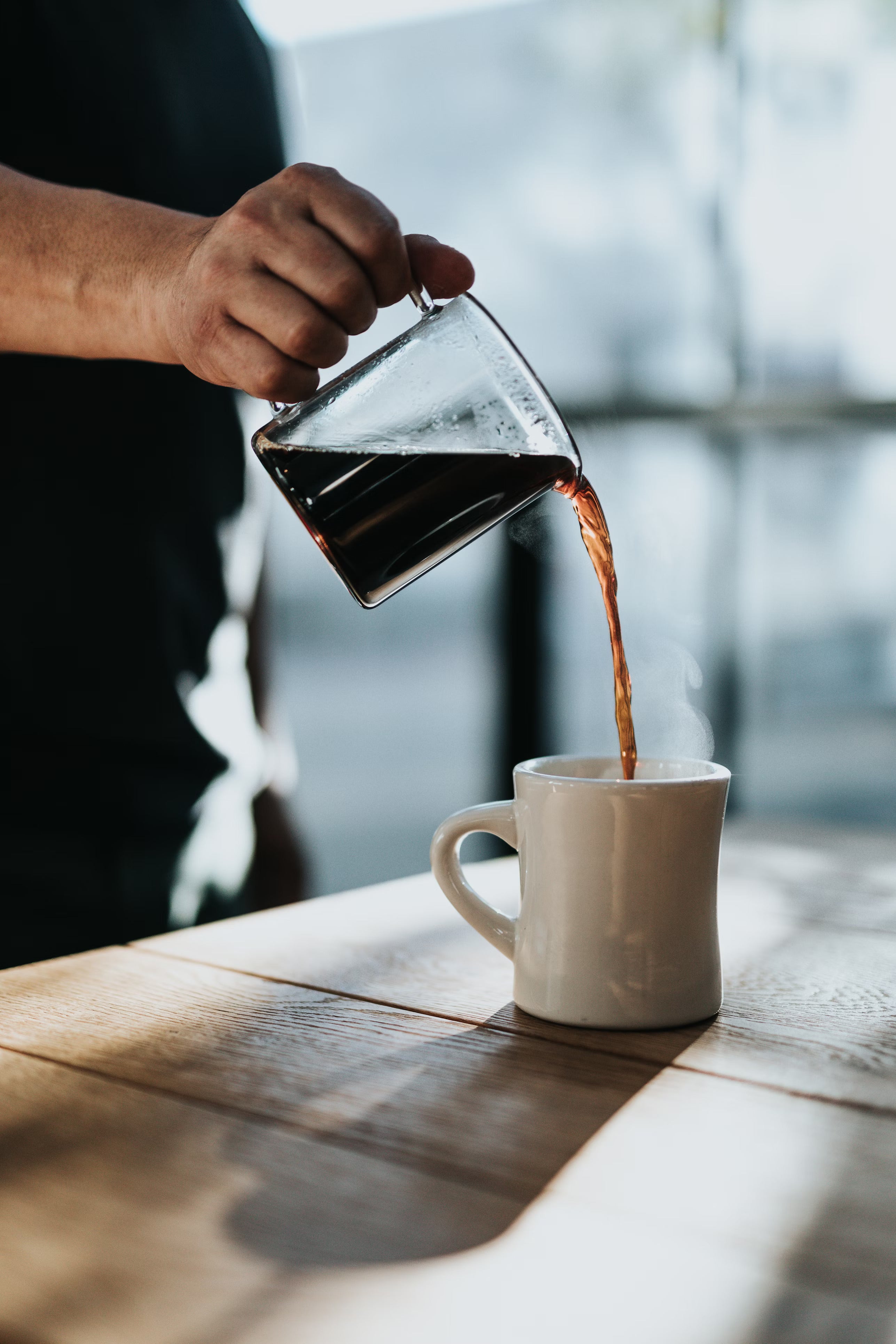 a man pouring a cup of coffee into a white mug